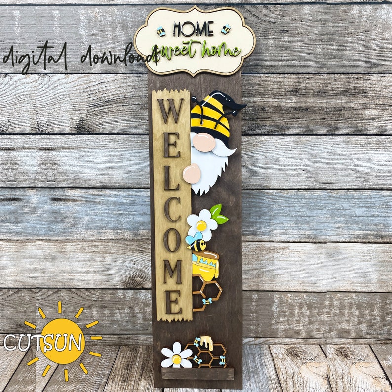 May include: Wooden welcome sign with a gnome peeking out from behind the letters. The sign is decorated with bees, honeycombs, and flowers. The sign reads "Welcome" and has a separate sign at the top that reads "Home Sweet Home".