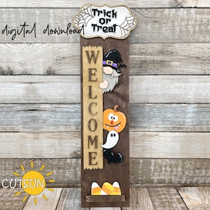 May include: A wooden welcome sign with a brown background and a vertical white sign that says "WELCOME". The sign has a witch, pumpkin, ghost, and bat decorations. The top of the sign has a white cloud with the words "Trick or Treat" and a spider web design.