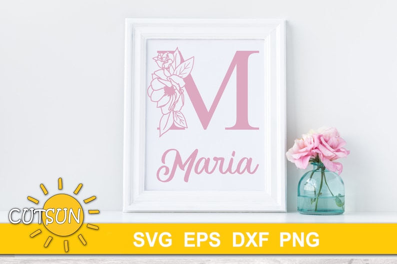 May include: A white frame with a pink floral design and the letter M, with the name Maria written below. The frame is sitting on a white surface.