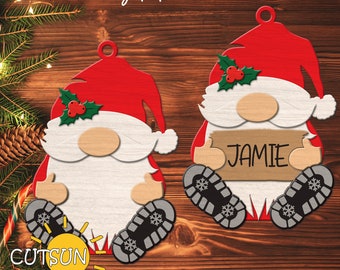May include: Two red and white Christmas gnome ornaments with a holly sprig on their hats. One gnome is holding a sign that says "JAMIE".
