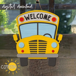 Può includere: Un cartello di benvenuto a forma di autobus scolastico giallo con la parola "WELCOME" in lettere nere e cerchi rossi su entrambi i lati della parola. Il cartello è appeso a una corda.