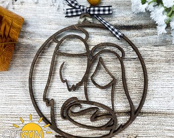 May include: A wooden Christmas bauble featuring a silhouette of the Holy Family. The bauble is brown and has a black and white checked ribbon attached to the top.