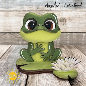 May include: A green frog figurine with large dark eyes, sitting on a lily pad base next to a white water lily flower. The text digital download is visible at the top, and the text CUTSUN with a sun icon is visible in the bottom left corner.