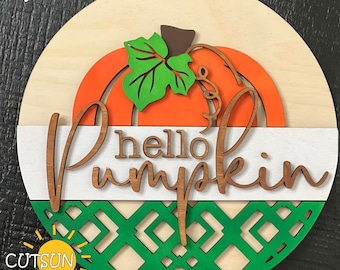 May include: A round wooden sign with a layered design featuring a pumpkin, the words "hello pumpkin", and a green geometric pattern. The sign is painted in orange, white, and green.