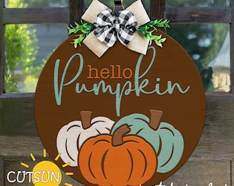May include: A brown round wooden door hanger with the text "hello pumpkin" in teal and orange. The door hanger has a bow with black and white checkered ribbon and green leaves. There are three pumpkins in the design, one orange, one teal, and one white.