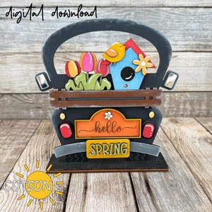 May include: A wooden truck cutout with a black base and a brown bed. The truck is decorated with flowers, a birdhouse, and the words "hello spring".