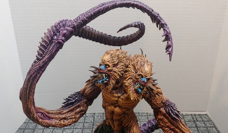 May include: A two-headed, brown and gold monster with a purple and brown tentacle-like arm. The monster has sharp teeth and blue eyes.