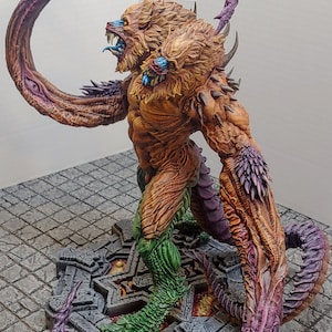 May include: A multi-headed, multi-limbed creature with a lion-like head and a green, scaly tail. The creature is painted in shades of brown, orange, and purple, and is standing on a stone base.
