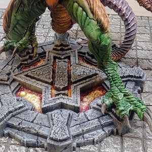 May include: A green and orange dragon figurine standing on a circular stone base with a glowing orange center. The base has intricate carvings and a star-shaped design.