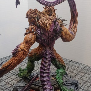 May include: A detailed, multi-colored, painted miniature of a monstrous creature with a long, curled tail and sharp claws. The creature is standing on a circular base with a textured surface.