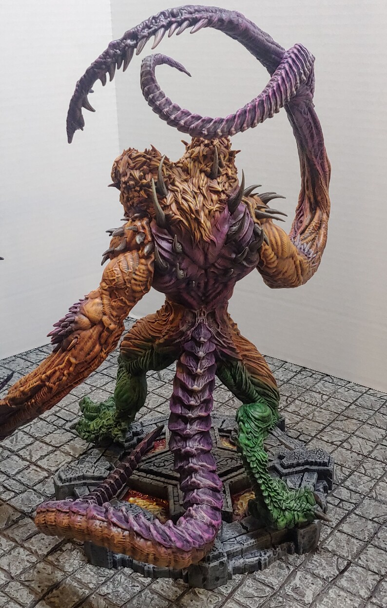 May include: A detailed, multi-colored, painted miniature of a monstrous creature with a long, curled tail and sharp claws. The creature is standing on a circular base with a textured surface.