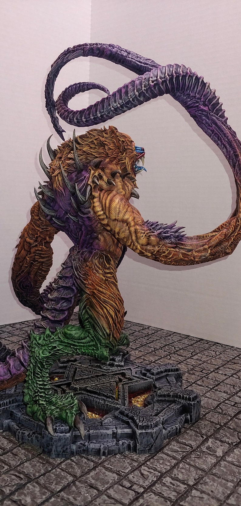 May include: A detailed, hand-painted miniature of a monstrous creature with a purple, green, and brown body. The creature has a long, curled tail and sharp claws. It is standing on a stone base with a lava-like design.
