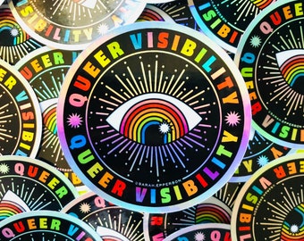 May include: A close-up of several round, iridescent stickers with the text "Queer Visibility" and a rainbow eye design. The stickers are arranged in a circular pattern.