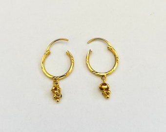 May include: A pair of gold hoop earrings with a small, dangling charm. The hoops are textured and the charms are made of small, round beads.
