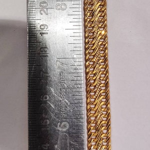 May include: A gold chain bracelet with a detailed, intricate design. The chain is measured against a ruler, showing its length.