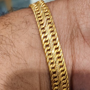 May include: A gold bracelet with a braided design. The bracelet is made of multiple strands of gold that are woven together to create a complex pattern.