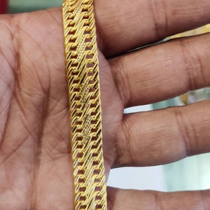 May include: A gold bracelet with a braided design. The bracelet is made of multiple strands of gold that are woven together to create a intricate pattern.
