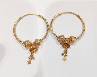 May include: A pair of gold hoop earrings with a dangling charm. The charm is a small bell with a beaded tassel.