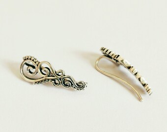 May include: A pair of silver earrings with a delicate, ornate design. The earrings are shaped like a curved leaf with intricate details.
