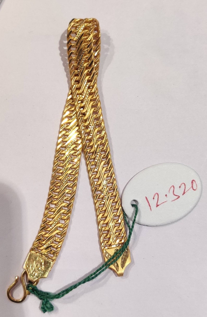 May include: A gold chain necklace with a textured, woven design. The chain is displayed on a white surface with a white oval tag that says "12,320".