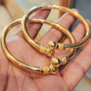 May include: Two gold bangles with a textured design and a round ball at the end of each bangle.