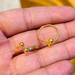 Puede incluir: Dos anillos de oro, uno con una forma redonda simple y el otro con dos bolas redondas en la banda.
