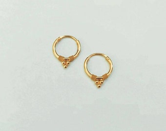 May include: A pair of gold hoop earrings with a small cluster of three gold beads hanging from the bottom of each hoop.