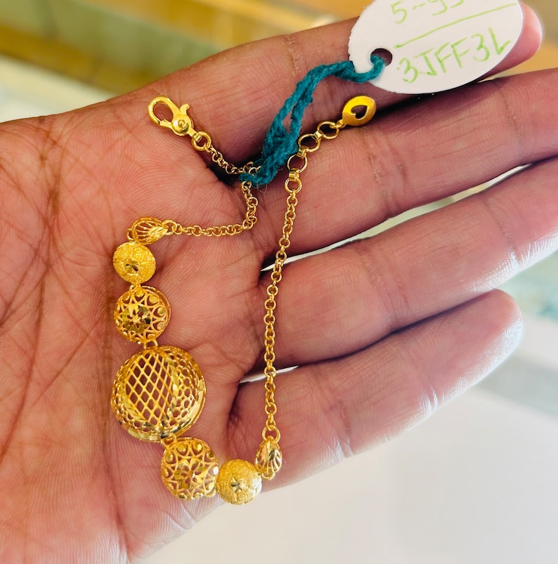 Pu&ograve; includere: Un braccialetto d'oro con una catena delicata e cinque ciondoli rotondi traforati. I ciondoli sono collegati da una catenina pi&ugrave; piccola. Il braccialetto ha una chiusura a moschettone.