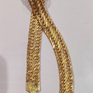 May include: A gold chain bracelet with a woven design. The bracelet has a hook clasp and is made of 18 karat gold.