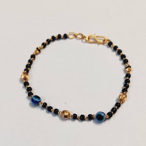 May include: A gold bracelet with black beads and blue evil eye charms. The bracelet has a gold clasp.