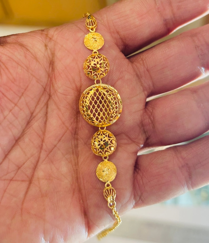 Pu&ograve; includere: Un braccialetto d'oro con una catena sottile e cinque ciondoli rotondi traforati. I ciondoli sono finemente decorati con motivi floreali e geometrici.