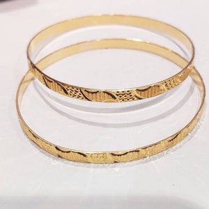 May include: Two gold bangles with a textured, patterned design. The bangles are stacked on top of each other.