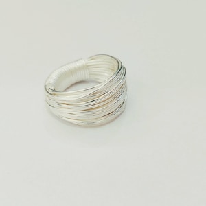 May include: A silver ring made of multiple thin wires woven together. The ring is wide and has a rounded shape.