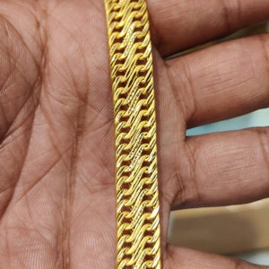 May include: A gold chain bracelet with a braided design. The chain is thick and has a shiny finish.