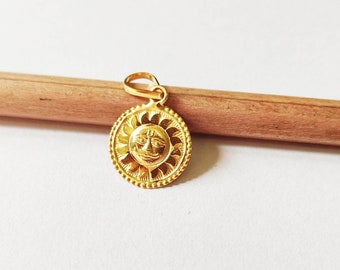 May include: A gold pendant featuring a sun with a face, surrounded by a decorative border.
