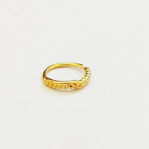 Può includere: Un piccolo anello per il naso color oro con un design a perline. L'anello è circolare e ha una chiusura a cerniera. Il design presenta una serie di piccole perline in rilievo sul davanti. Il gioiello è posto su uno sfondo bianco.