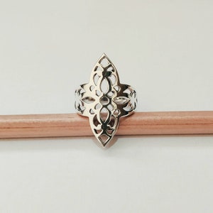 May include: A silver ring with a delicate, intricate design resembling a flower or star. The ring is made of a thin metal and has a cutout pattern.