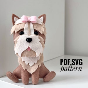 May include: A brown and white felt Yorkshire Terrier dog toy with a pink bow. The toy is sitting on a white surface. PDF, SVG pattern.