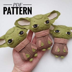 May include: Three felt plush toys of a popular fictional character, each in different sizes. The toys are green with large eyes and brown and pink clothing. The toys are on a hand, with the text "PDF PATTERN" above them.