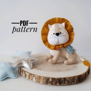 May include: PDF pattern for a felt lion toy. The lion is sitting on a wooden slice and has a light brown body, a white face, and a brown mane. The lion is wearing a blue scarf.
