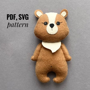 May include: A brown felt bear with a white felt collar and black eyes. The bear is standing on a gray surface. The text "PDF, SVG pattern" is written in black above the bear.