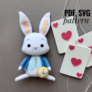 May include: White felt bunny rabbit toy with blue jacket and a pocket watch. The bunny has pink ears and black eyes. The image also includes four white felt cards with pink hearts on them. The text "PDF, SVG pattern" is written in black on a white background.