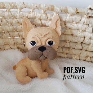 Könnte beinhalten: Ein beigefarbenes Stofftier aus Filz in Form eines französischen Bulldoggen, das auf einer weißen, flauschigen Oberfläche sitzt. Das Spielzeug hat schwarze Augen, eine schwarze Nase und braune Filzohren. Der Text "PDF, SVG pattern" ist in der unteren rechten Ecke des Bildes sichtbar.