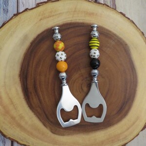 May include: Two silver bottle openers with bee-themed bead handles. One handle has yellow and black striped beads, the other has white and yellow honeycomb pattern beads.