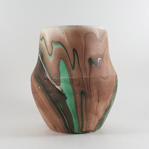 May include: A decorative vase with a distinctive, swirling pattern. The vase showcases a mix of brown, green, and white hues, producing a marbled appearance. It has a broad base and a somewhat narrower top, with a smooth, glossy finish.
