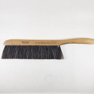 May include: A wooden drafting brush with long, dark, stiff bristles. The light-colored wooden handle features a small hole at the end for hanging and is stamped with the text 'STERLING' and 'NO 3511 MADE IN U.S.A.' along the side of the handle.
