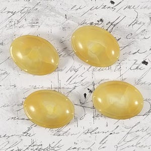 May include: Four oval, yellow cabochon gemstones with a marbled effect. The stones are arranged in a circular pattern against a background of handwritten script. Each stone is approximately 2.5 cm in length.