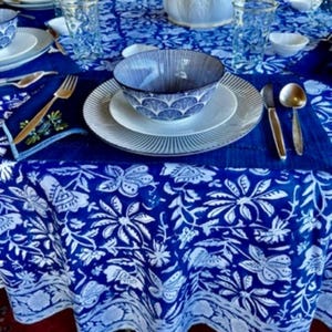 Peut inclure: Une table dress&eacute;e avec une nappe &agrave; motifs floraux bleus et blancs. L'ensemble comprend des assiettes blanches, des bols &agrave; motifs bleus et des couverts dor&eacute;s. Des verres transparents et un vase d&eacute;coratif sont &eacute;galement pr&eacute;sents.