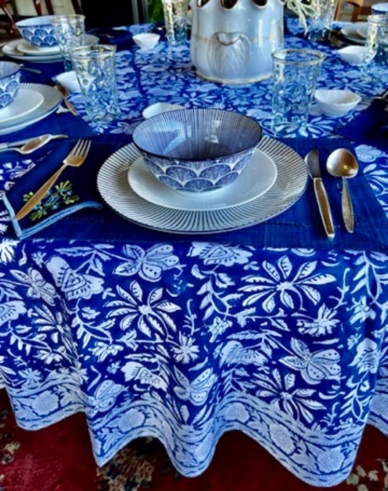 Peut inclure: Une table dress&eacute;e avec une nappe &agrave; motifs floraux bleus et blancs. L'ensemble comprend des assiettes blanches, des bols &agrave; motifs bleus et des couverts dor&eacute;s. Des verres transparents et un vase d&eacute;coratif sont &eacute;galement pr&eacute;sents.
