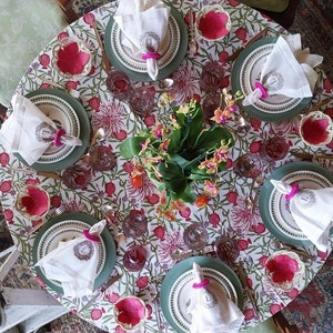 Puede incluir: Un mantel de mesa floral con un patr&oacute;n rosa y verde. Hay siete cubiertos con servilletas blancas, platos verdes y cuencos rosas. Las servilletas est&aacute;n dobladas y tienen un anillo con la letra 'L' en ellas.